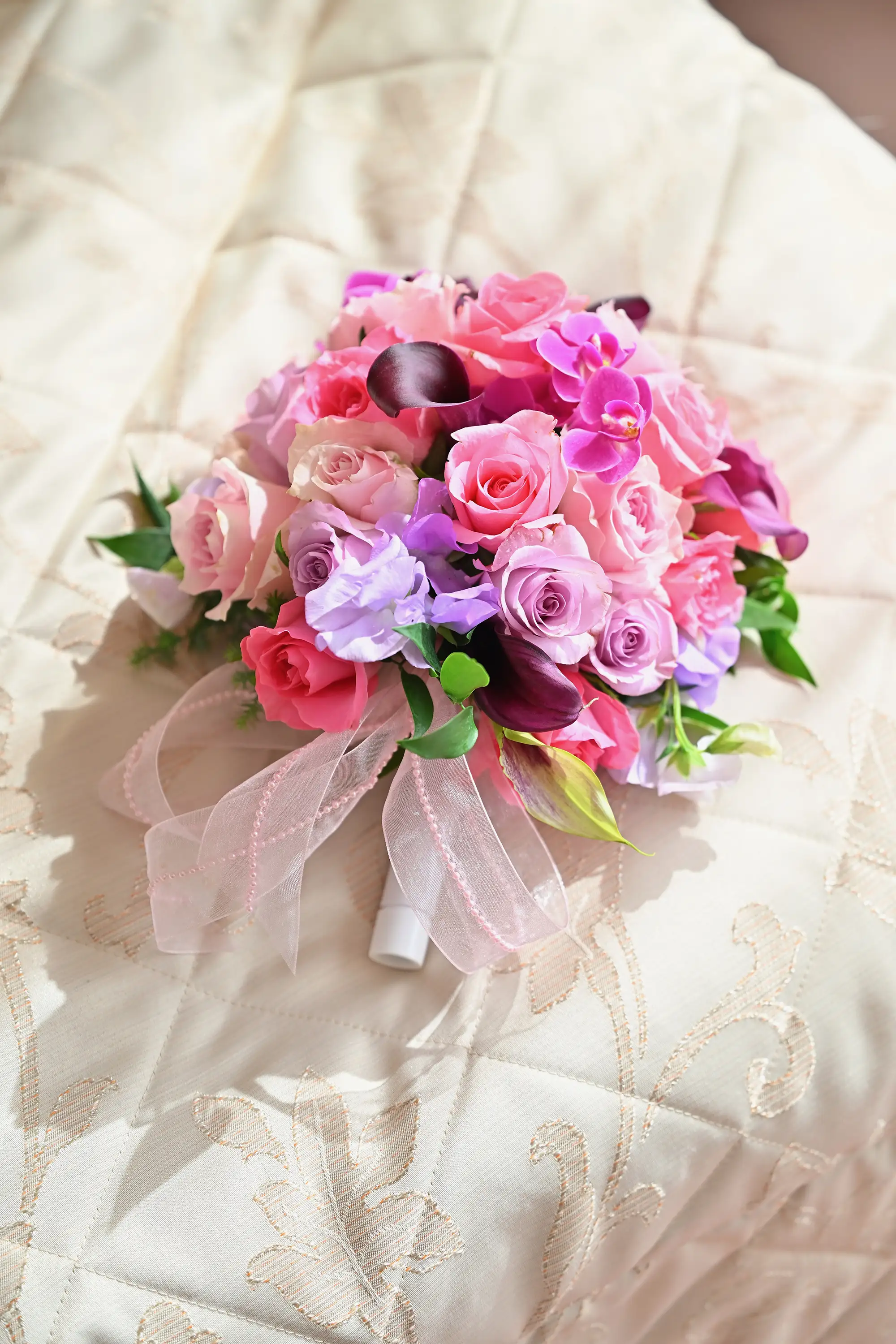 窓からの自然光に照らされた、ベッドの上に置かれたピンク系のブライダルブーケ