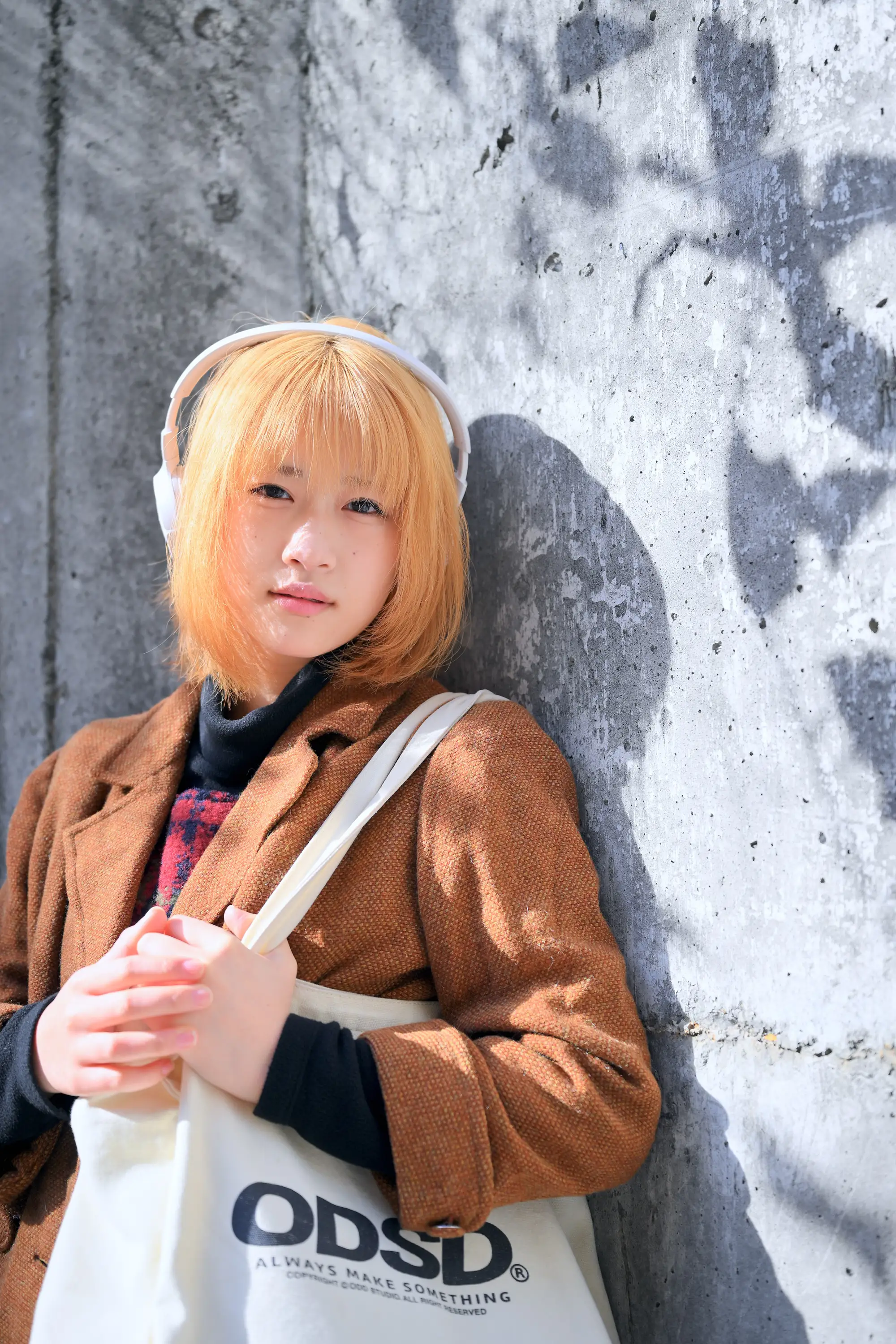 コンクリートの壁にもたれかかりヘッドフォンで音楽を聞く女性のポートレート