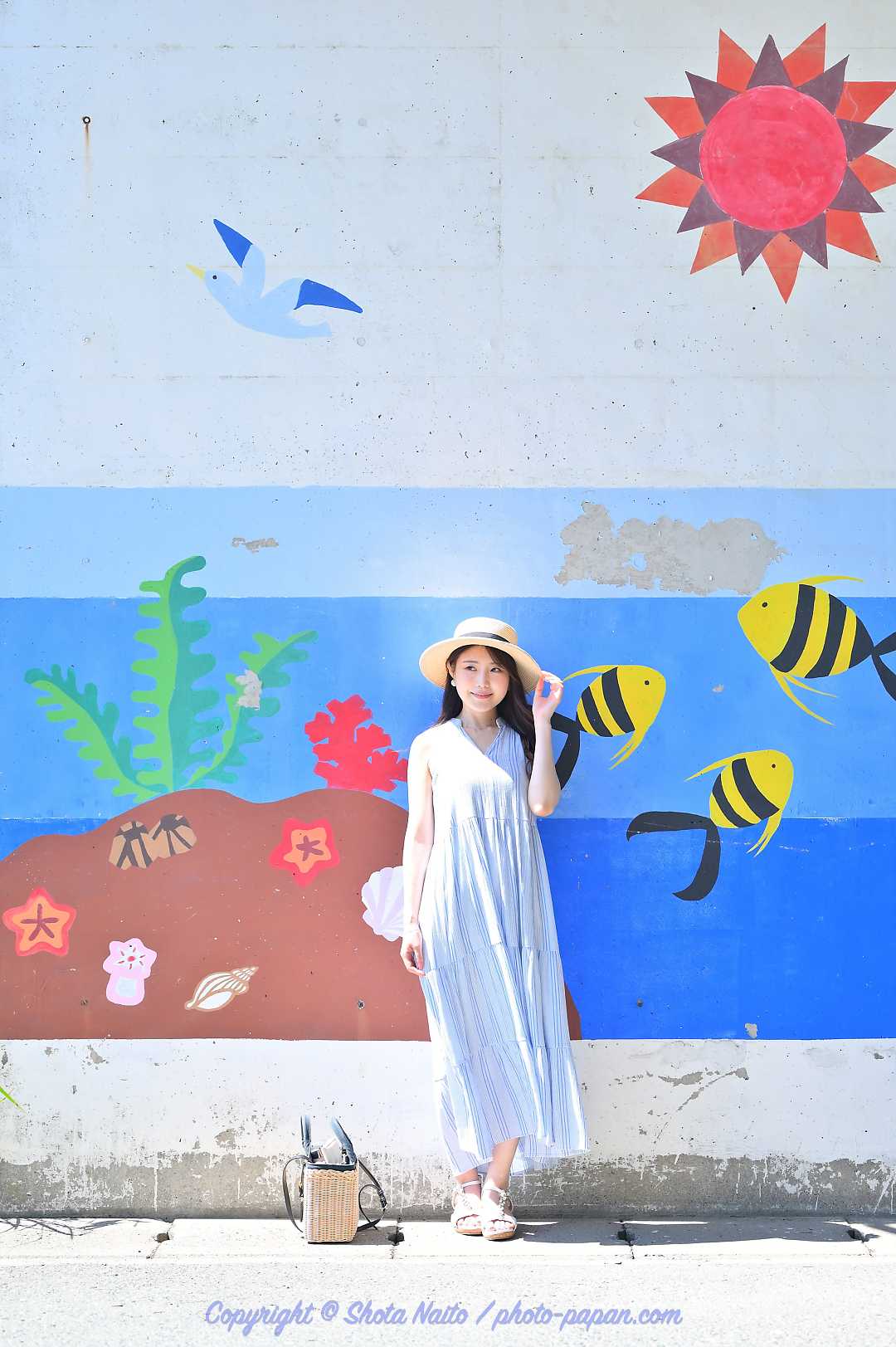 かわいい海の生き物壁画を背にした麦わら帽子の女性